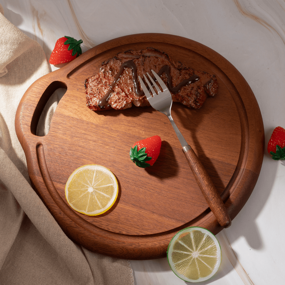 Multi-functional wooden cutting board with steak, strawberries, and lemon slices on marble countertop.