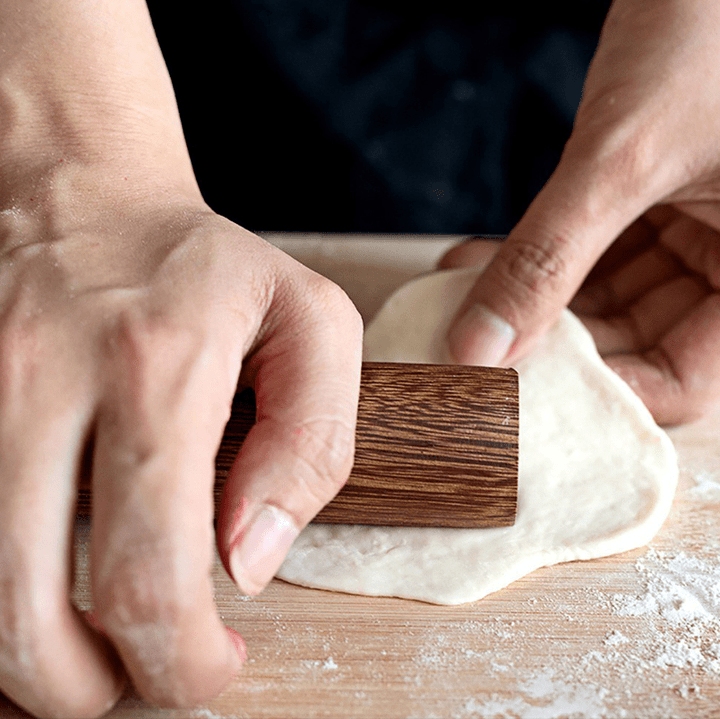 Person using a no paint and no wax wooden rolling pin to roll out dough for pastries on a floured surface.