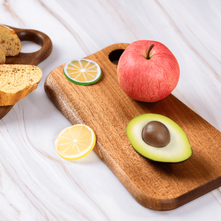 Walnut wood ring-shaped mini cutting board with an apple, avocado, and lemon slices for baby food preparation.
