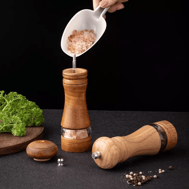 Two-tone rubberwood spice grinder set with salt being added, alongside fresh parsley on a dark background.