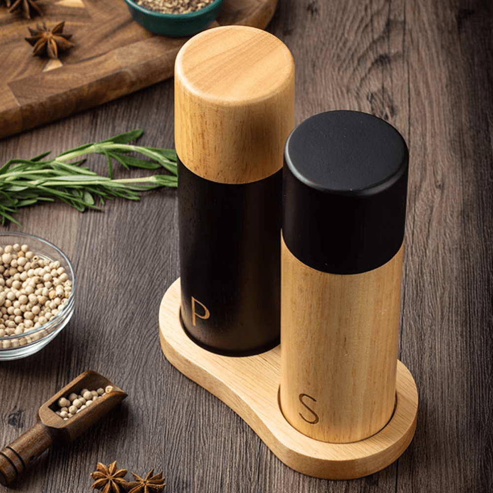 Sea salt and pepper grinder combo set in natural rubber wood on a wooden table with spices.