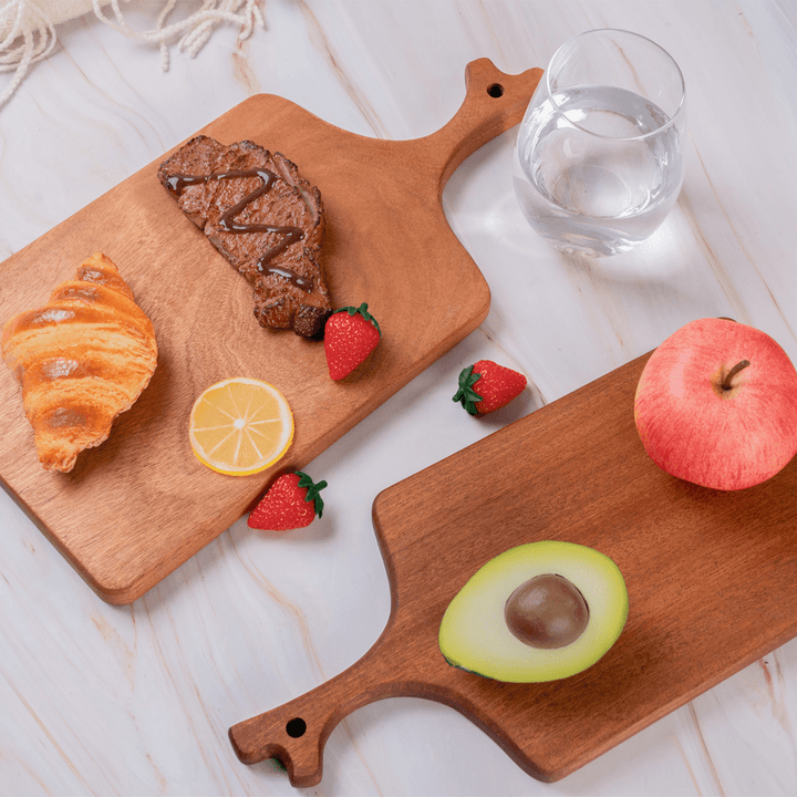 Artistic multi-functional cutting board with foods like croissant, steak, fruits, and a glass of water on a stylish kitchen countertop.