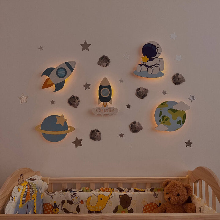 Personalized wooden wall light set for baby's room featuring rockets, planets, and stars, creating a cozy nighttime atmosphere.