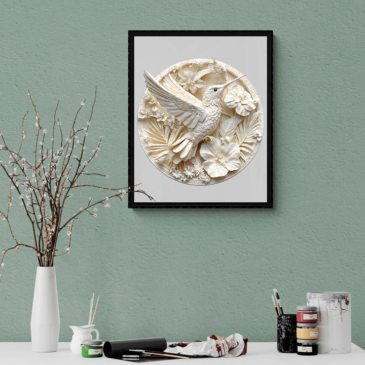 3D wall art of a hummingbird surrounded by flowers, framed in black, displayed on a green wall.