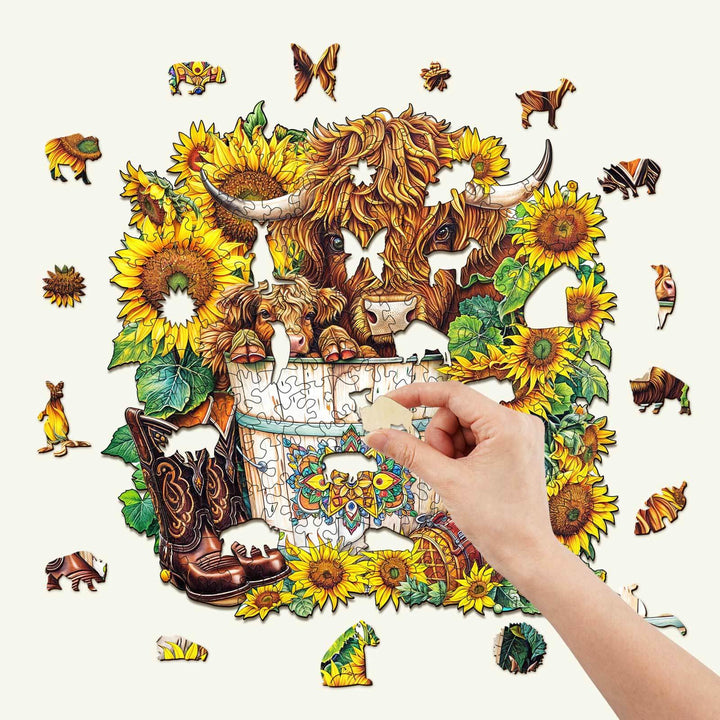 Hand placing a piece in the Sunflower Pasture wooden jigsaw puzzle filled with vibrant sunflowers and animals.