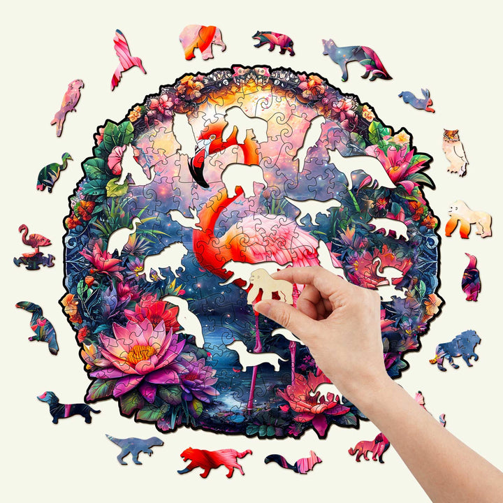 Hand placing a piece in an Elegant Flamingo wooden jigsaw puzzle featuring colorful wildlife and flowers.