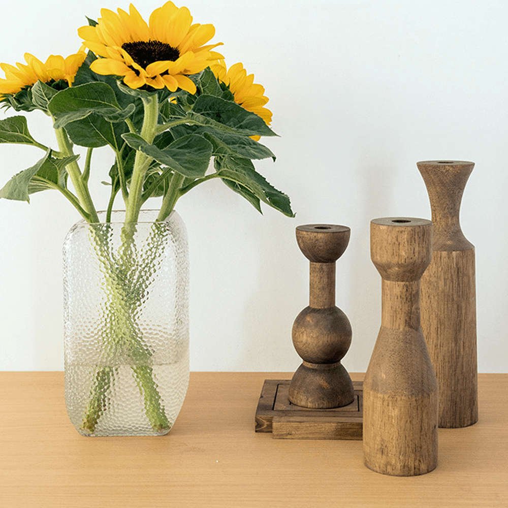 Wooden candle holders alongside a vase of sunflowers on a wooden table, adding elegance to home decor.