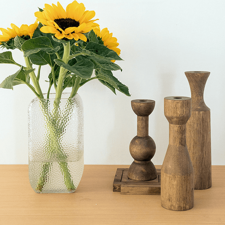 Wooden candle holders alongside a vase of sunflowers on a wooden table, adding elegance to home decor.
