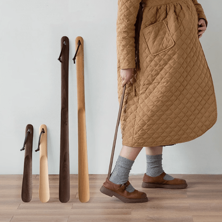 A collection of walnut shoe horns in various sizes displayed beside a person dressed in a quilted brown coat.