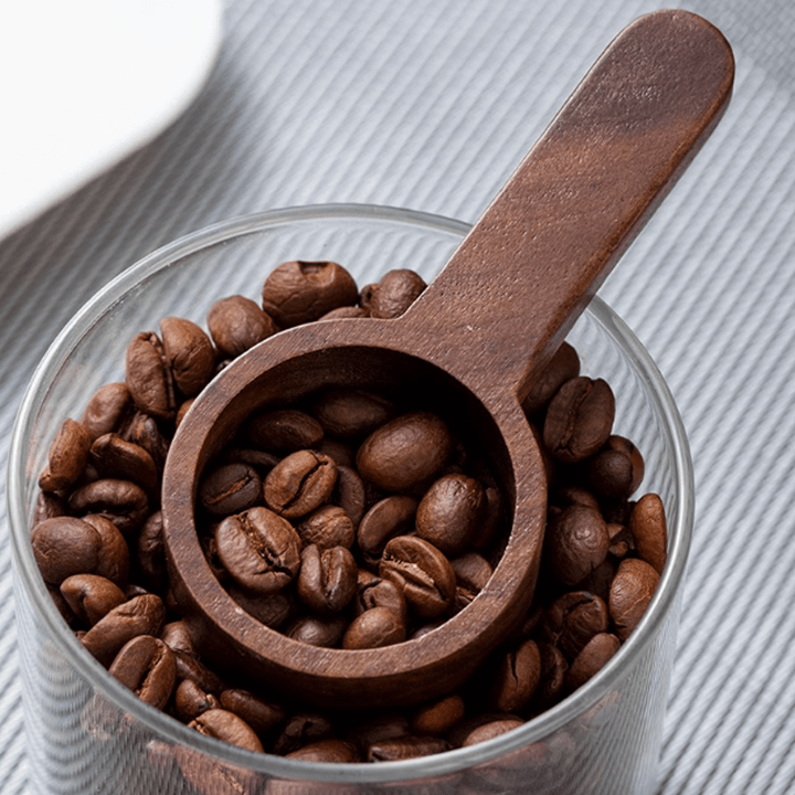 Wooden measuring spoon resting on coffee beans in a glass container, ideal for precise cooking measurements.