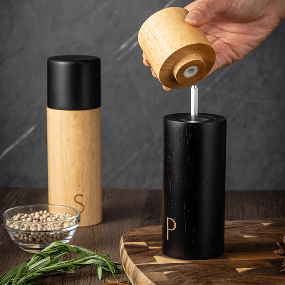 Natural rubber wood sea salt and pepper grinder combo set with a person using the black grinder.