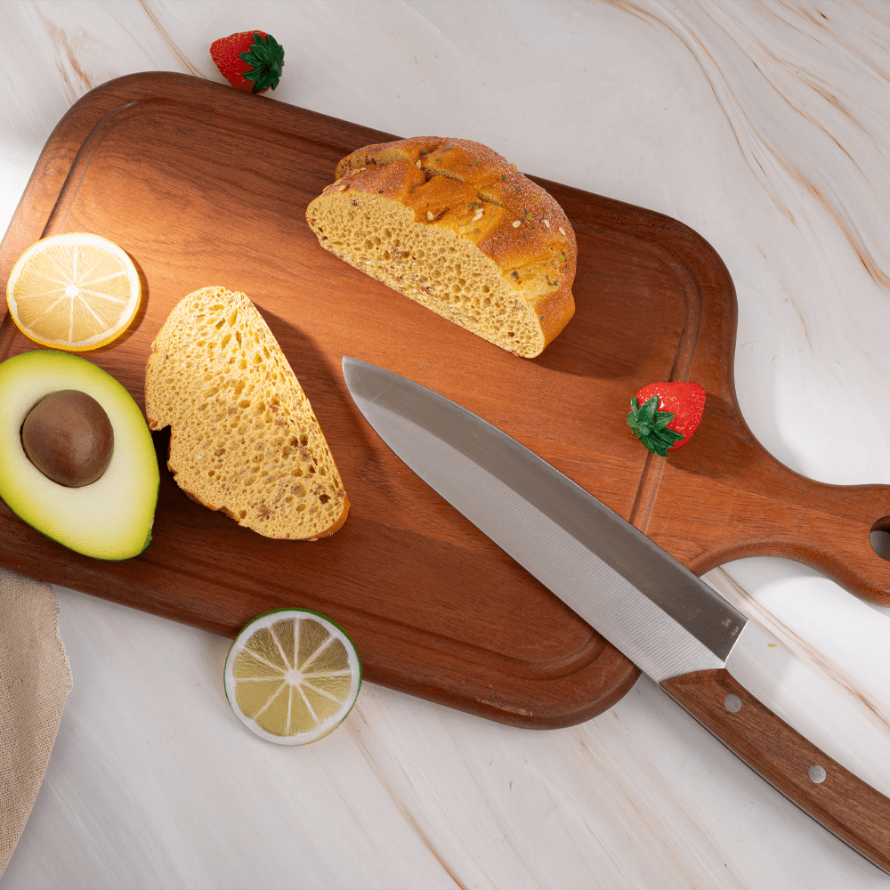 Multi-functional cutting board with sliced bread, avocado, lemon, and knife on a stylish kitchen countertop.