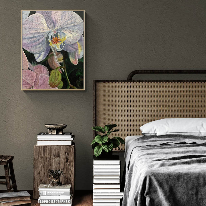 Framed orchid artwork by Marianne K Palmer displayed above a cozy bed with plants and books in a stylish bedroom setting.