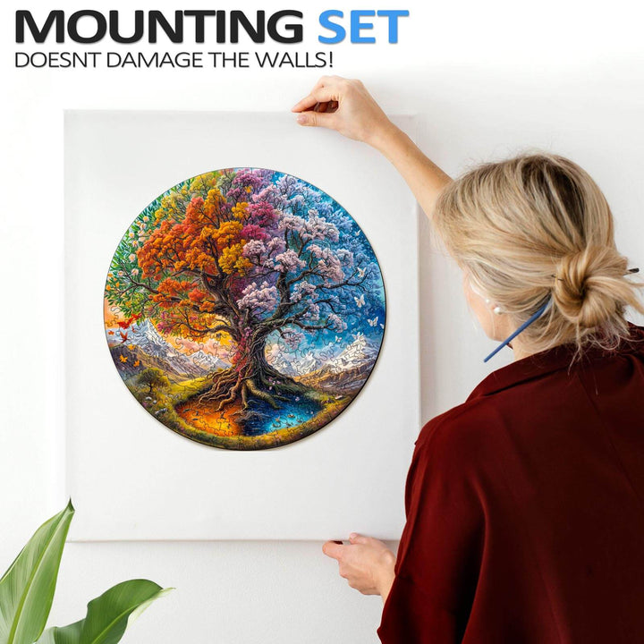Woman using a damaging-free mounting set to display a colorful Seasonal Tree of Life jigsaw puzzle on a wall.