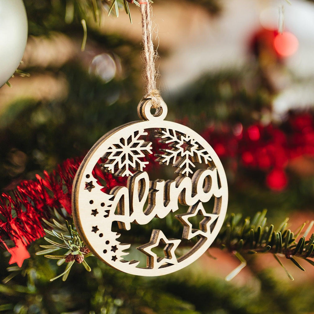 Personalized wooden Christmas ornament with the name 'Alina', snowflakes, and stars, hanging on a decorated tree.