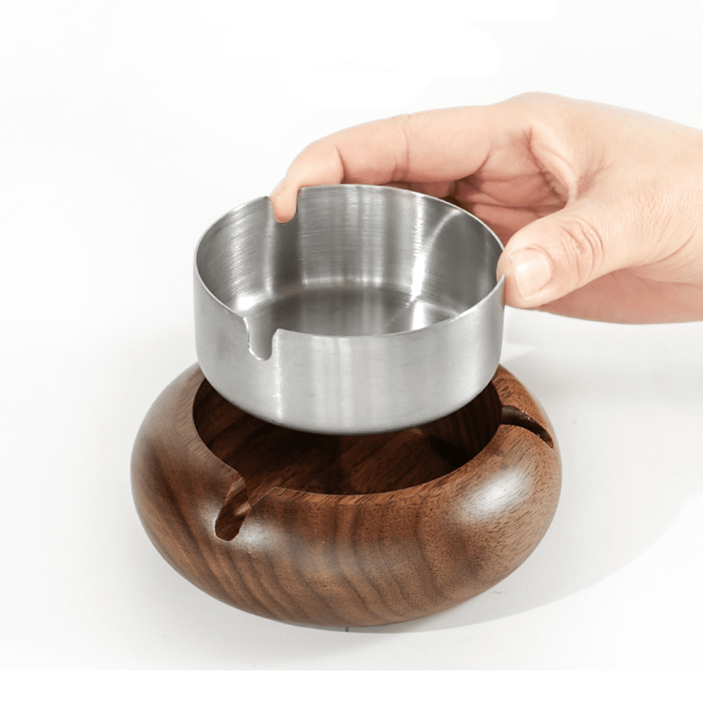 Hand holding a stainless steel liner above a round walnut ashtray, showcasing its modern design and natural beauty.