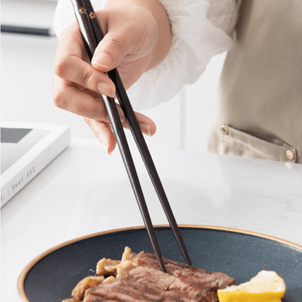Person using non-slip sakura pointed-tip wooden chopsticks to pick up food from a plate.