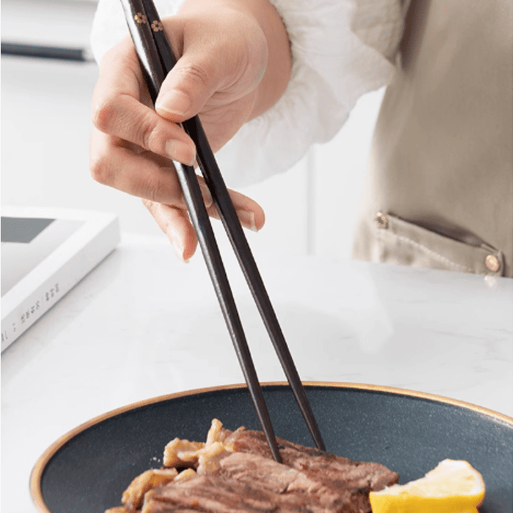 Person using non-slip sakura pointed-tip wooden chopsticks to pick up food from a plate.