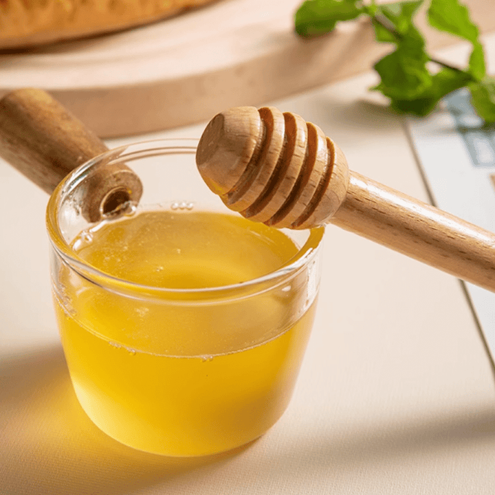 Beechwood stirring stick next to a glass of honey, perfect for natural drinks and healthy stirring.