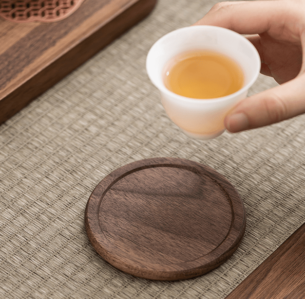 Minimalist walnut coaster on a dining table with a hand holding a cup of tea.