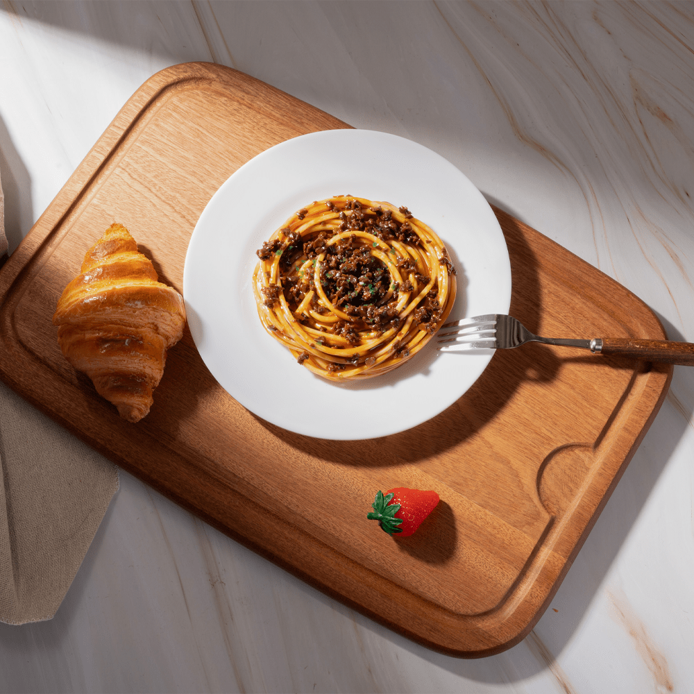 Multi-functional cutting board showcasing a plate of spaghetti, croissant, and fresh strawberry on a stylish surface.