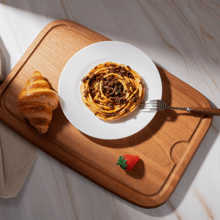 Multi-functional cutting board showcasing a plate of spaghetti, croissant, and fresh strawberry on a stylish surface.