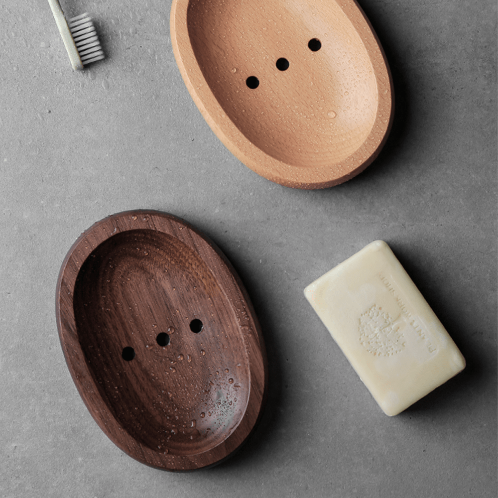 Two natural wooden soap boxes in log style, one dark walnut and one light beech, with a bar of soap and toothbrush.