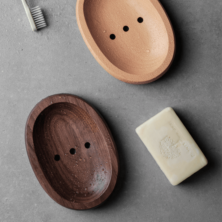 Two natural wooden soap boxes in log style, one dark walnut and one light beech, with a bar of soap and toothbrush.