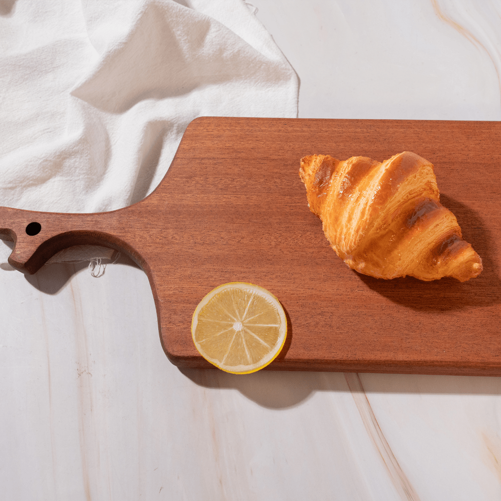 Multi-functional cutting board in branch design with croissant and lemon slice on a smooth surface.