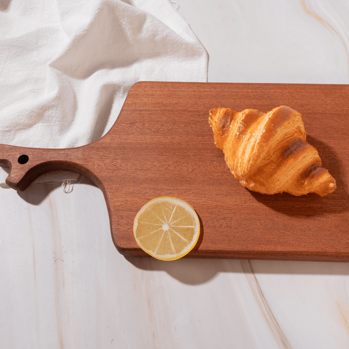 Multi-functional cutting board in branch design with croissant and lemon slice on a smooth surface.