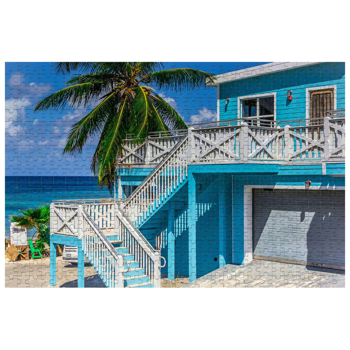 Summer Style 500/1000 piece puzzle featuring a vibrant blue beach house with palm trees adjacent to the ocean.