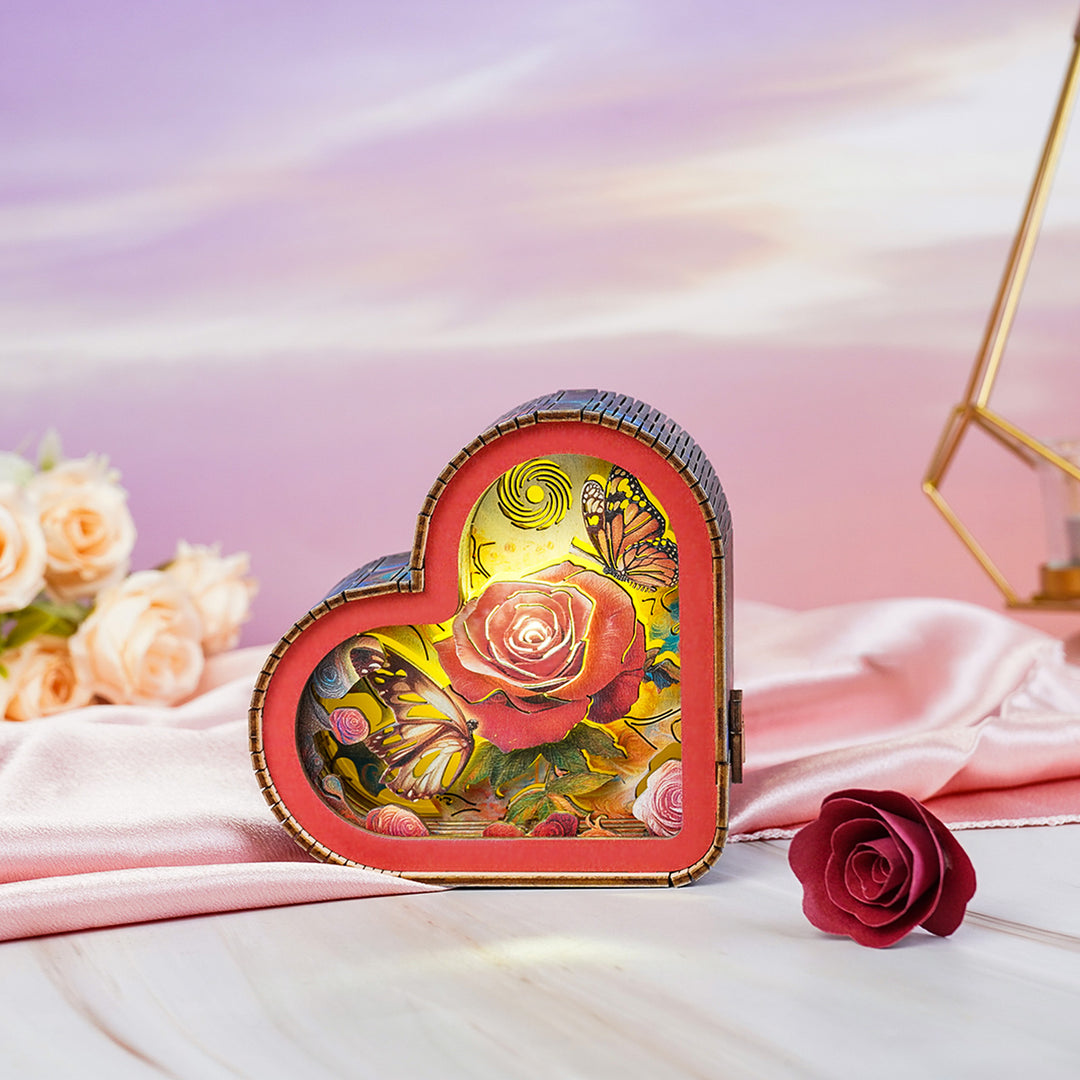 Heart-shaped 3D wooden puzzle night light featuring a rose and butterflies, glowing softly on a pink silk background.