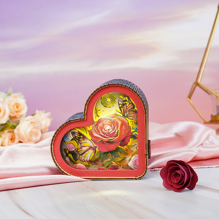 Heart-shaped 3D wooden puzzle night light featuring a rose and butterflies, glowing softly on a pink silk background.