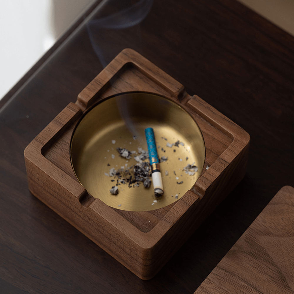 Square wooden ashtray with brass liner, featuring a cigarette and ashes, perfect for modern spaces.