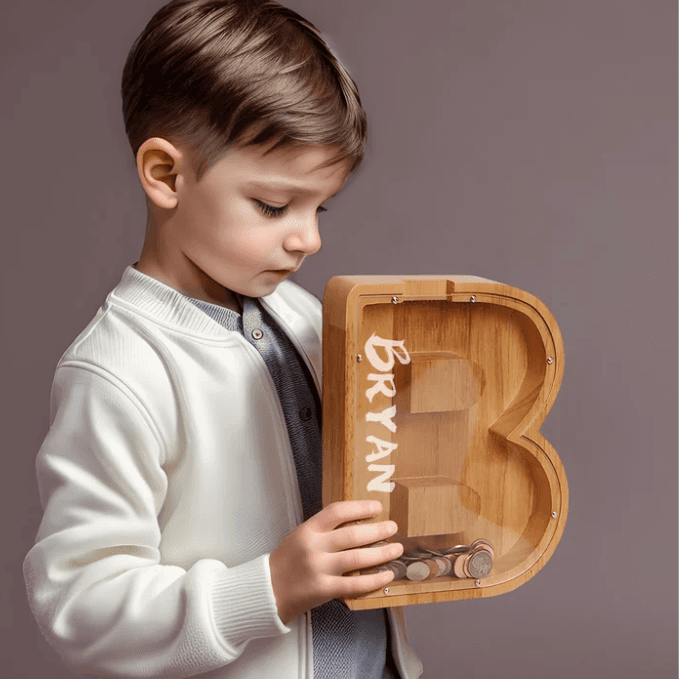 Child holding a personalized wooden letter piggy bank, promoting financial awareness and savings for kids.