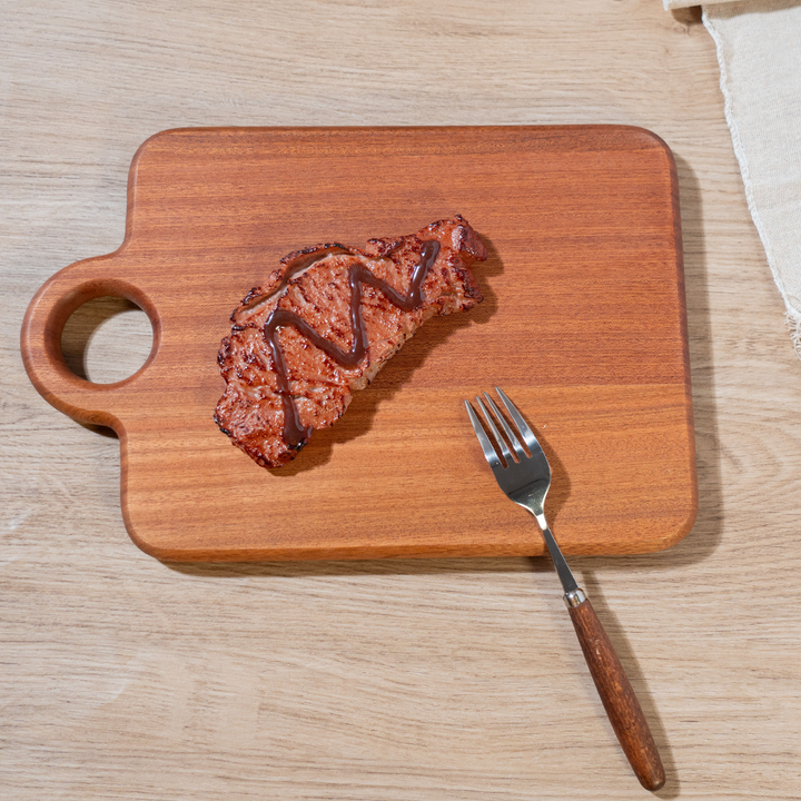 Ebony heavy-duty cutting board with a grilled steak and fork, showcasing its elegant design and practical use in the kitchen.
