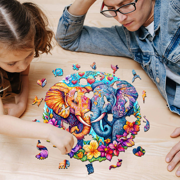 Two people assembling a colorful Snuggling Elephant wooden jigsaw puzzle surrounded by vibrant pieces on a wooden table.