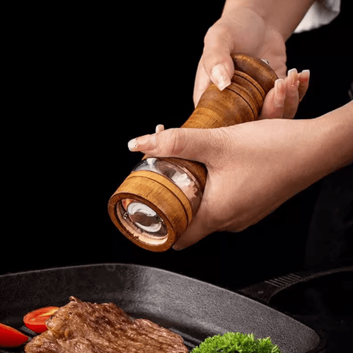 Person using a rubberwood two-tone spice grinder over a sizzling steak, showcasing its unique design and functionality.