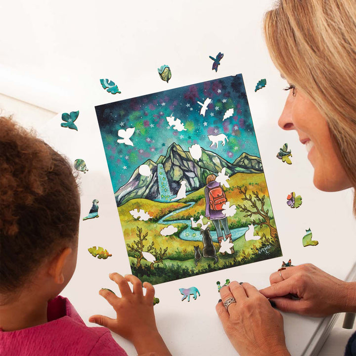 A woman and child admire the 'Mountains and Stars' artwork by Kathryn Fedora, surrounded by colorful puzzle pieces.
