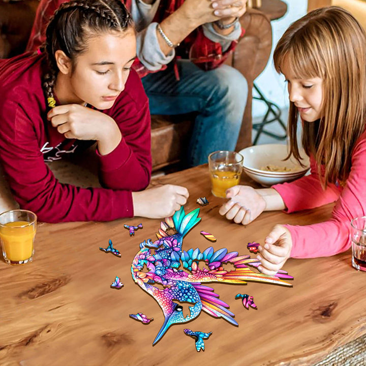 Two girls enjoying a Jewel hummingbird wooden jigsaw puzzle on a table, promoting focus and cognitive skills.