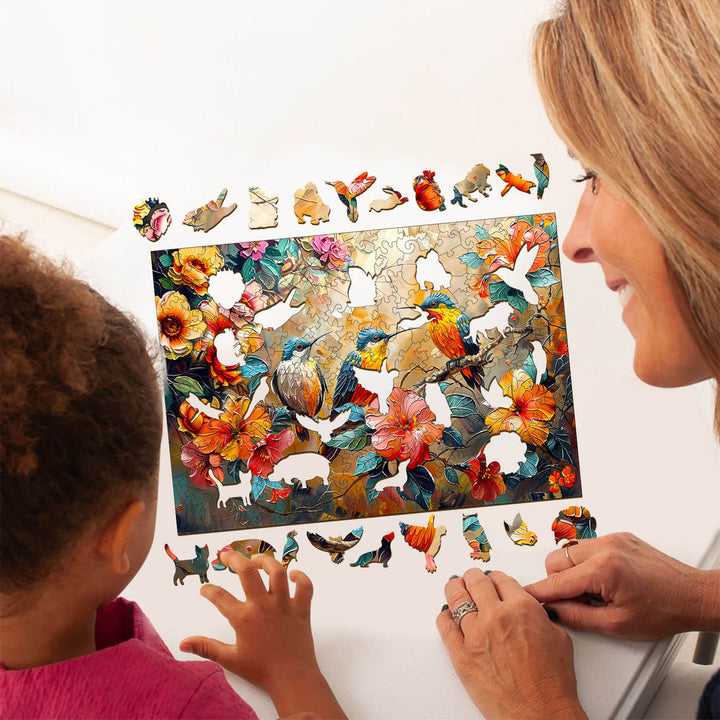 A woman and child assembling a Hummingbird Garden wooden jigsaw puzzle while surrounded by colorful puzzle pieces.