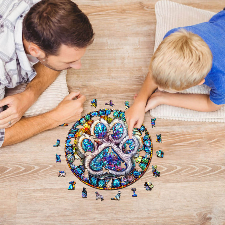 Father and son enjoying a colorful stained glass paw prints wooden jigsaw puzzle on a wooden floor.