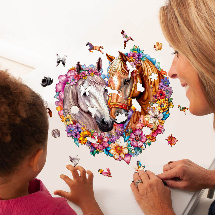 A child and adult working on the 'Horse in Love' wooden jigsaw puzzle featuring two horses and colorful flowers.