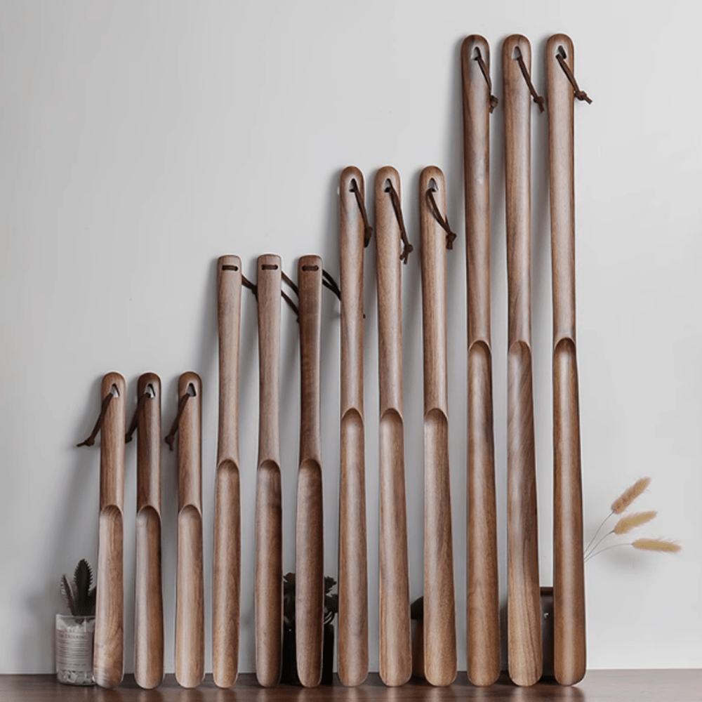 A collection of wooden shoe horns in various sizes, crafted from natural walnut, displayed on a wall.