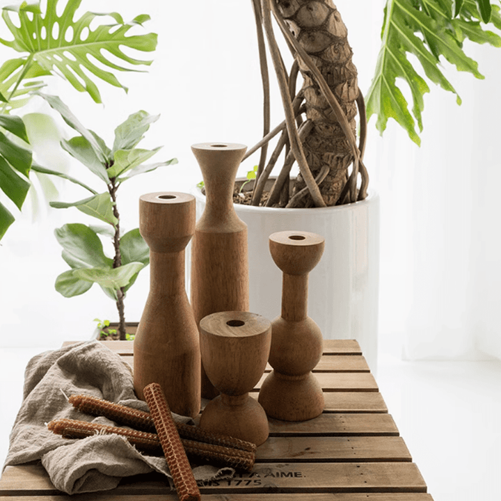 American retro wooden candle holders on a wooden table with green plants in the background.