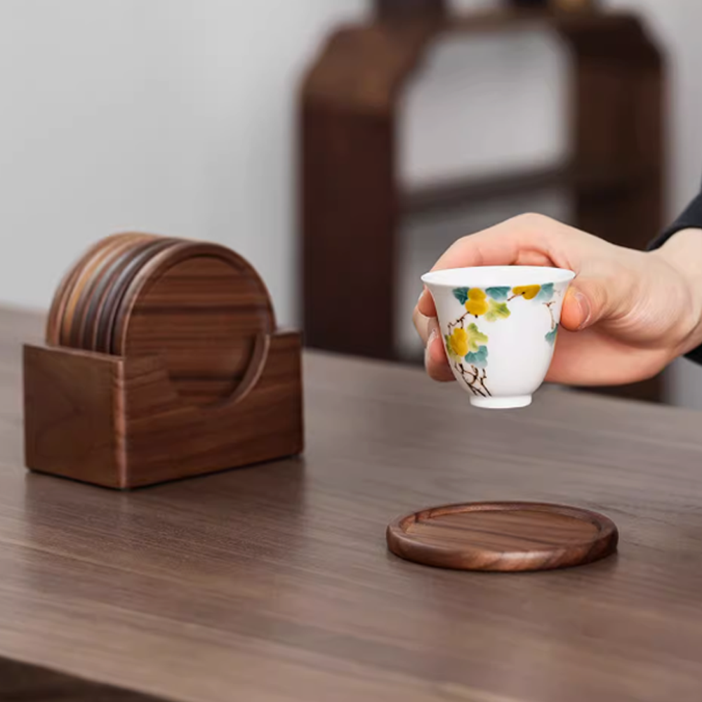 Minimalist walnut coasters on a wooden table, with a hand holding a ceramic cup, showcasing elegance and natural beauty.