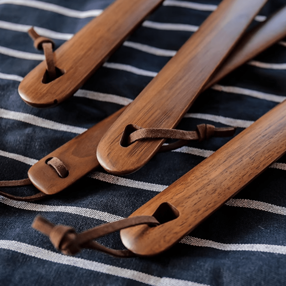 Set of walnut shoe horns with leather ties on a striped fabric background, showcasing natural elegance and craftsmanship.