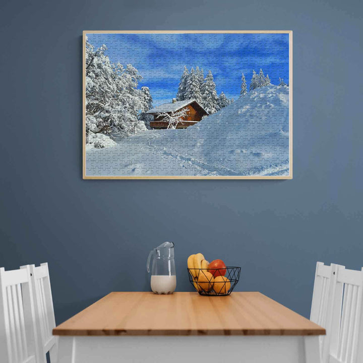Snow Cabin 500/1000 Piece Puzzle displayed in a cozy dining room setting with snow-covered trees and blue sky.