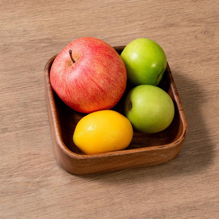 Organic wooden plate holding a red apple, green apples, and a lemon on a wooden table.