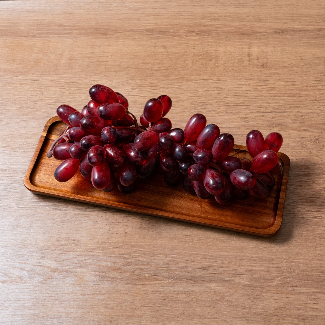 Organic wooden tray holding fresh red grapes on a wooden surface, ideal for storing various items.